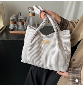 Detail of light gray corduroy tote bag featuring a brown leather fashion patch logo