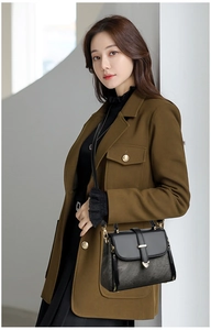 Detail of a chic black handbag featuring a gold heart-shaped metal buckle on a green coat