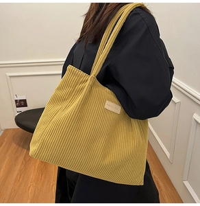 Detail of yellow corduroy tote bag featuring an embroidered fashion label and texture