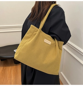 Détail du sac cabas en velours côtelé jaune moutarde porté par un mannequin en intérieur