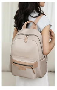 Detail of a beige nylon backpack with brown leather trim worn by a model in a studio