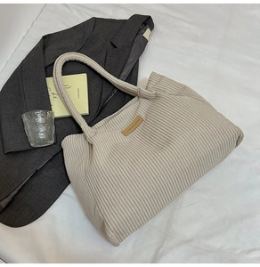 Detail of beige corduroy tote bag with leather logo patch and textured vertical stripes
