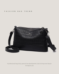 Detail view of black crossbody bag with three zipper compartments and crocodile texture