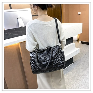 Detail of a black quilted puffer tote bag worn by a model in an indoor setting
