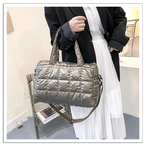 Detail of metallic quilted tote bag with adjustable brown strap shown on a model