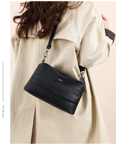 Detail view of black crocodile pattern crossbody bag with metal kangaroo logo and strap