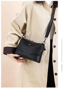 Black crocodile embossed leather crossbody bag shown on a model with a beige coat