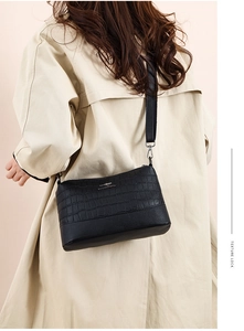 Close-up of black crossbody bag with crocodile texture and metal logo on a model