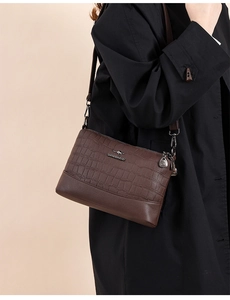 Detail of dark brown leather crossbody bag with crocodile texture and metal logo