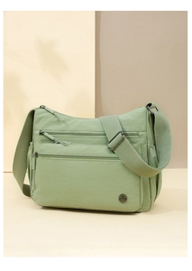 Detail view of light green nylon crossbody bag showing multiple zip pockets and wide strap