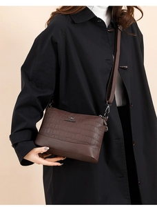 Detail of dark brown crossbody bag with crocodile texture and adjustable strap