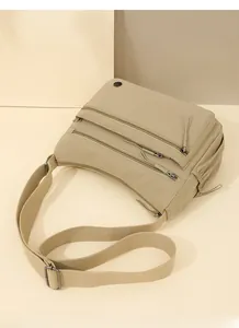 Detail of khaki nylon crossbody bag showing multiple functional front zipper pockets