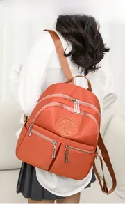 Detail eines orangen Nylon-Rucksacks mit Herz-Logo und Reißverschlusstaschen am Modell