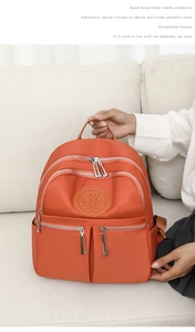 Detailansicht des orangen Nylon-Rucksacks mit Reißverschlusstaschen und Logo-Prägung