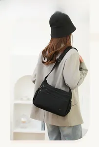 Detail of black nylon shoulder bag with multiple zippered layers and sleek metal logo