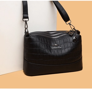 Detail of black faux leather crossbody bag featuring crocodile texture and silver zipper