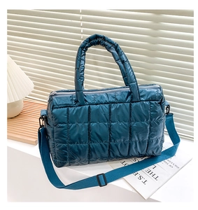 Detail of teal blue quilted puffy handbag featuring cylindrical handles and broad strap