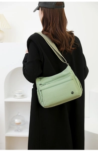 Close-up of light green nylon crossbody bag with multi-pocket zipper design and wide strap