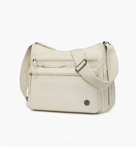 Detailed 45-degree angle view of cream nylon crossbody bag with multi-zipper pockets