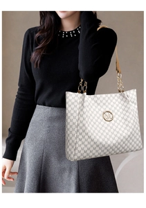 Detail of cream tote bag with repetitive M pattern and gold chain leather strap