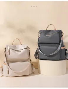 Detail view of nylon backpacks in cream and charcoal with leather handles and zip pockets