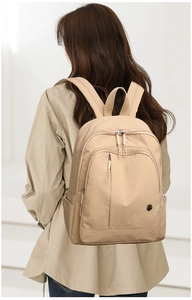 Rear view of a beige oxford cloth backpack with multiple zipper pockets on model