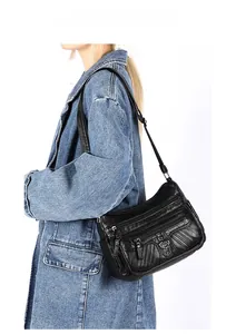 Side view of black faux leather crossbody bag with multiple zippers and heart buckle