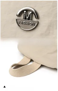Detailed shot of silver M FASHION logo and soft woven handle on a beige backpack