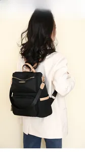 Rear view of a model wearing a black nylon backpack with leather handles and gold zippers