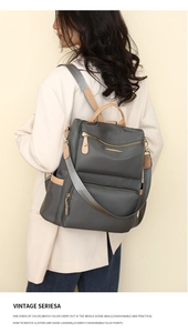 Side view of dark grey nylon backpack with brown leather trim worn by model on shoulder
