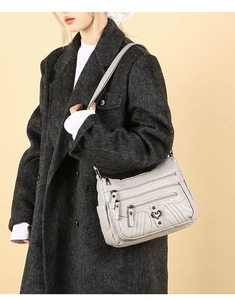 Detail of light gray multi-pocket crossbody bag featuring heart-shaped hardware