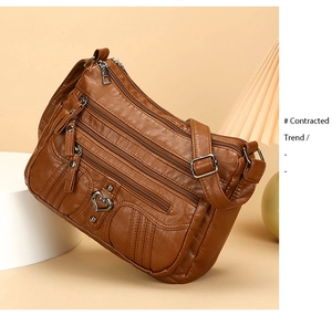 Detail of a brown leather multi-pocket crossbody bag with a heart metal charm and zipper
