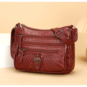Detail of burgundy multi-pocket crossbody bag with heart buckle and textured leather