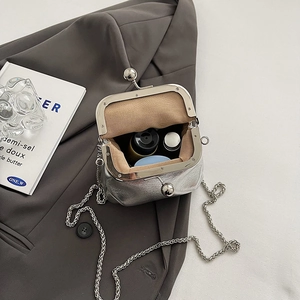 Petit sac bandoulière argenté avec fermoir à baiser et chaîne sur veste grise