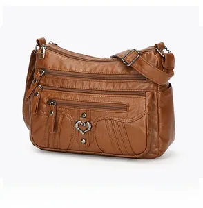 Detail of a brown soft leather crossbody bag with multiple zip pockets and heart charm