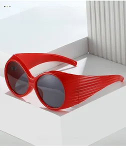 Detail of red oval sunglasses featuring textured ribbed temples and glossy modern frame