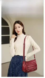 Detail view of burgundy faux leather crossbody bag with multiple zip pockets on model