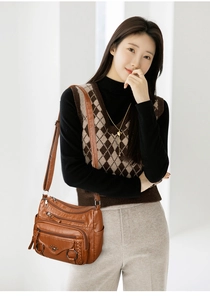 Close-up of brown soft leather crossbody bag featuring multi-zipper compartments and metallic rings