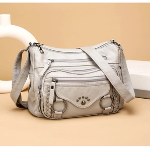 Detail of grey pebbled faux leather bag showing multiple zippers and cat paw rivet design