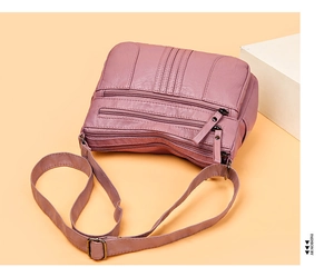 Detail of soft dusty pink leather shoulder bag with multiple zippered pockets and metal hardware