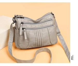 Macro detail of grey soft leather shoulder bag with multi-layer zippers and decorative stitching