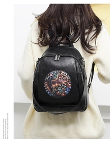 Detail view of the black leather backpack featuring a vintage elephant relief and floral art
