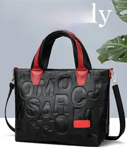 Detail of black pebbled leather tote with red accents and embossed letter patterns