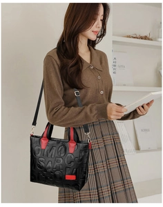 Detail of black tote bag with embossed letters and contrasting red handles and side strap