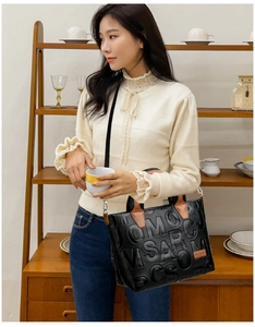 Detail of black tote bag featuring embossed letters and contrasting brown leather straps