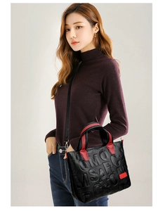 Detail of embossed letter pattern on black leather tote bag with red brand plaque
