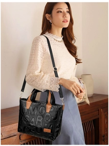 Close-up of black embossed leather tote with letter patterns and brown handles on a model