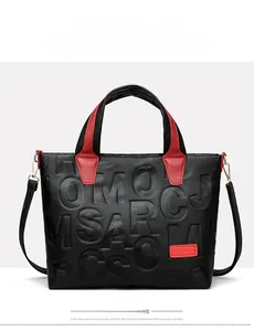 Detail of red handles on black tote bag with embossed letters and gold metal hardware