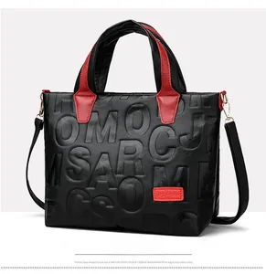 Close-up of black lychee leather tote bag with red embossed letters and golden hardware
