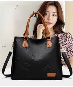 Detail of embossed black leather tote with floral patterns and gold hardware